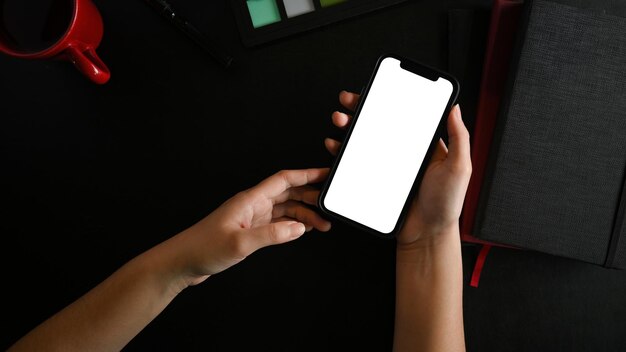 Closeup vrouwelijke handen holen mobiele telefoon wit scherm mockup op zwarte werktafel bovenaanzicht plat lag