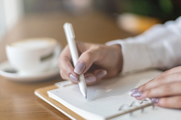 Closeup vrouwelijke handen maken aantekeningen op papier in Kladblok gebruik pen tafel cafetaria schrijven dagboek planning diary