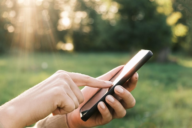 Closeup vrouwelijke handen met smartphone natuur achtergrond vrouw persoon mobiele telefoon zonsondergang buitenshuis