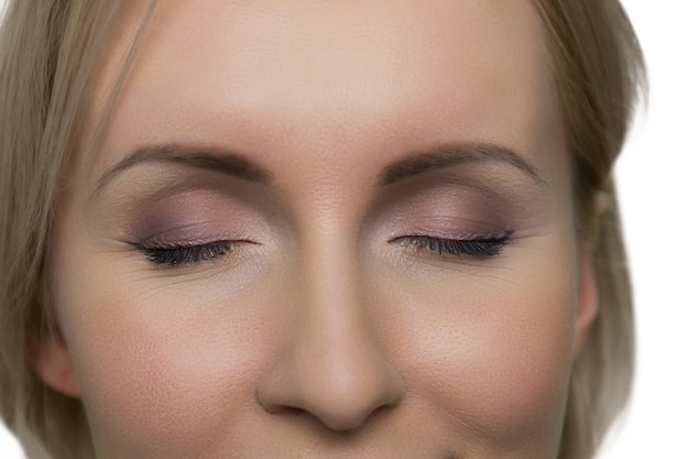 Closeup vrouwen gezicht met gesloten ogen en make-up op witte muur