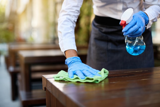 Photo closeup of waitress cleaning tables with disinfectant