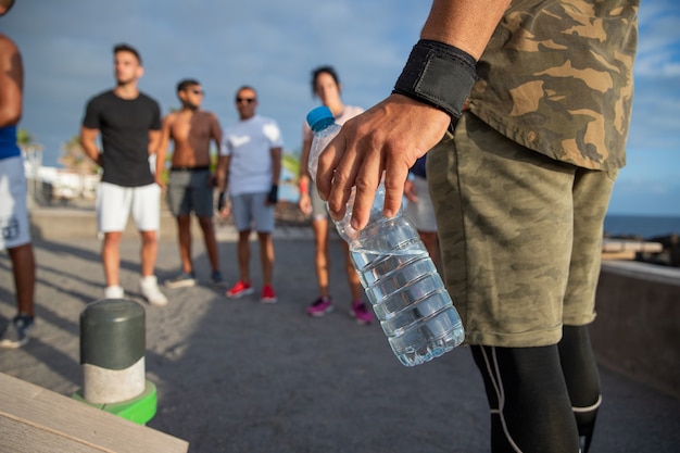 closeup on the water bottle held by a man during an outdoor work out with a group of athletes