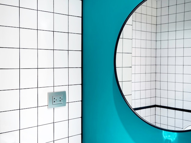 Closeup white ceramic tiles with grid pattern bathroom wall\
view reflected in a big round shape of the mirror on blue wall\
background minimal style