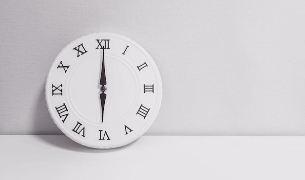 Photo closeup white clock for decorate in 6 o'clock on wood desk in black and white tone