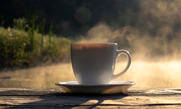 Closeup of a white cup of coffee on a wooden table on a background of water