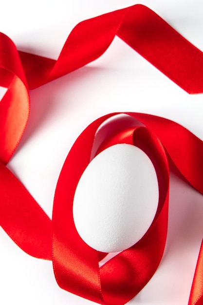 Closeup white egg with red silk ribbon easter symbol on light background Place for text