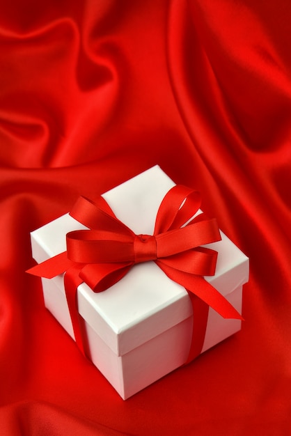 Closeup of white gift box with bow ribbon over smooth red satin background