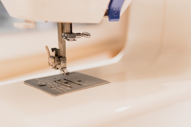 Closeup of a white sewing machine foot on blurred background.