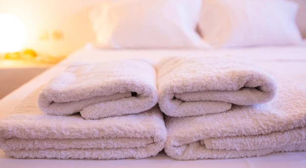 Closeup of white towels on a bed on a blurry with warm light background