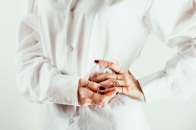 Closeup of white woman's hands with various rings around her waits, white shirt,  .