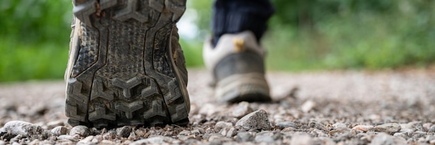 Immagine ampia vista del primo piano dei piedi maschili in scarpe da trekking che camminano su un sentiero di ghiaia