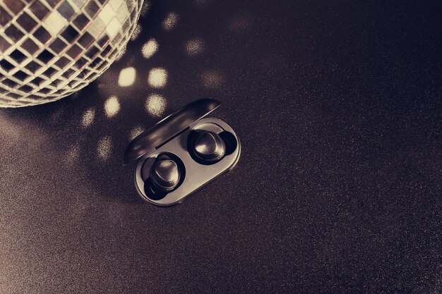 充電ケースのワイヤレスヘッドフォンのクローズアップ黒の背景にディスコボール高品質
