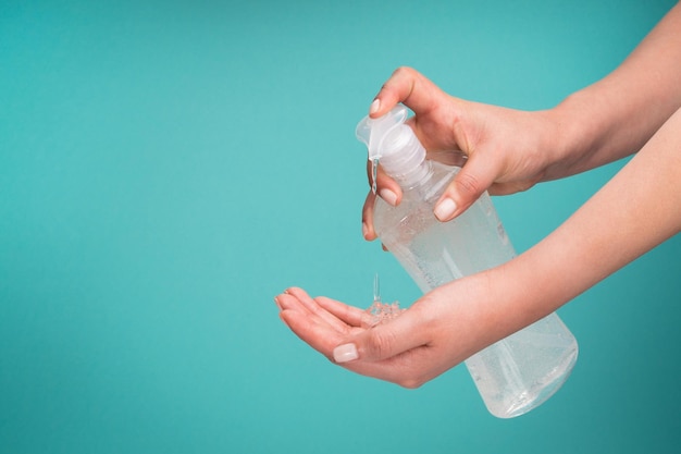 Closeup of a woman applying hand sanitizer against Coronavirus on a turquoise background