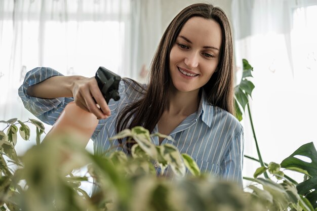 青いシャツのクローズアップの女性は植物、植物ケアの概念をスプレーします