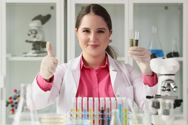 Closeup of woman chemist holding test tubes and showing thumbs up sign science education