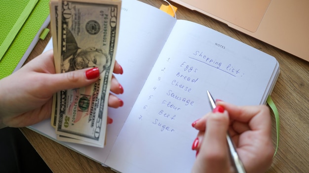 Photo closeup of woman counting money and making shopping list in notepad earned money savings and