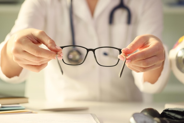 Photo closeup of woman doctor giving pair of black glasses to patient eyesight test and correction