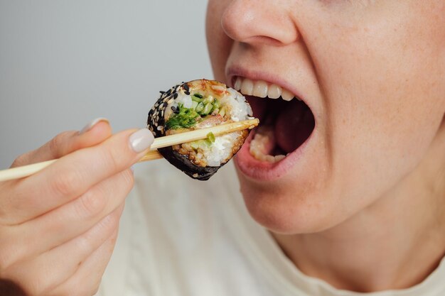 Foto closeup di una donna che mangia un rotolo di sushi con le bacchette