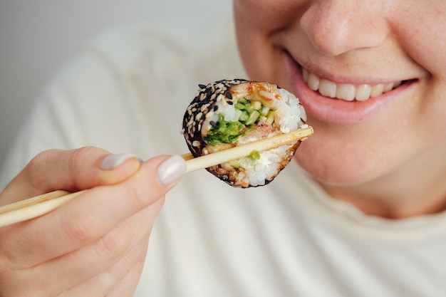 Photo closeup of woman eating sushi roll with chopsticks