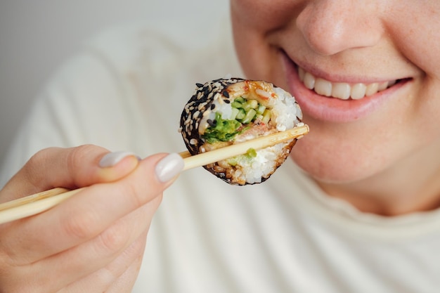 Foto closeup di una donna che mangia un rotolo di sushi con le bacchette