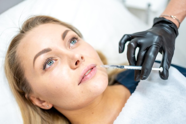 Closeup of woman face and hand in surgical glove holding syringe near her lips ready to receive beauty treatment Injection cosmetology aesthetic surgery lips augmentation and correction concept