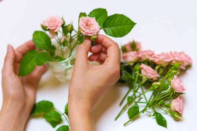 Closeup of woman florists hand making bouquet of pink roses on a light table beautiful cute bouquet ...