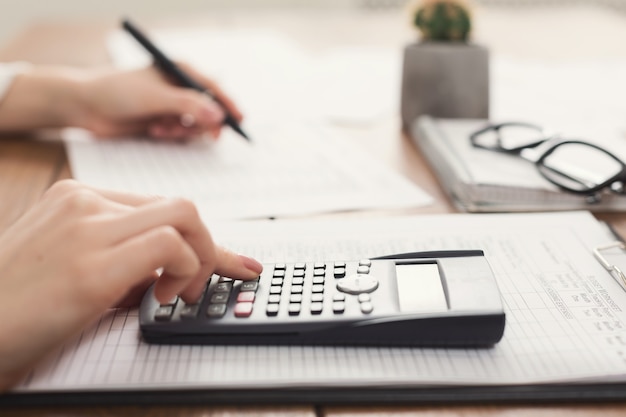 Closeup of woman hand counting account on calculator and writing in documents. Financial background, count and pay an account, copy space, selective focus