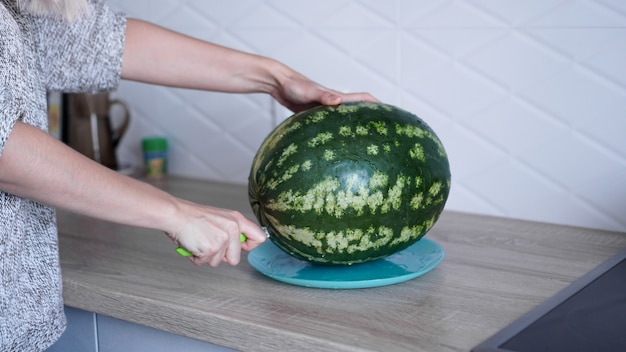 Closeup of woman hand cutting fresh watermelon in the kitchen