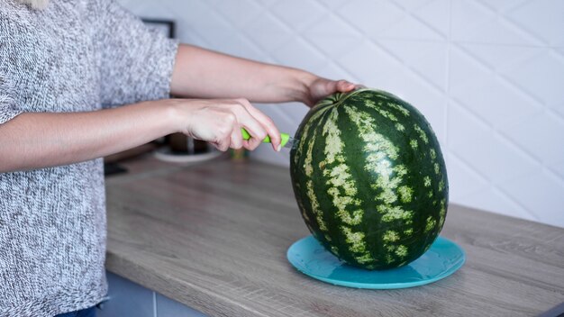 Closeup of woman hand cutting fresh watermelon in the kitchen