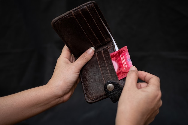 赤いコンドームと黒革の財布を持つクローズアップ女性手