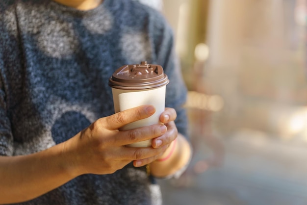 Closeup of woman hand holding disposable take away paper cup of hot coffee with copy space.