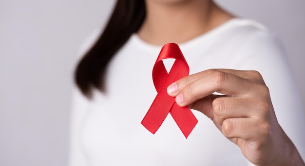 Closeup woman hand holding red ribbon HIV, world AIDS day awareness ribbon. Healthcare and medicine concept.