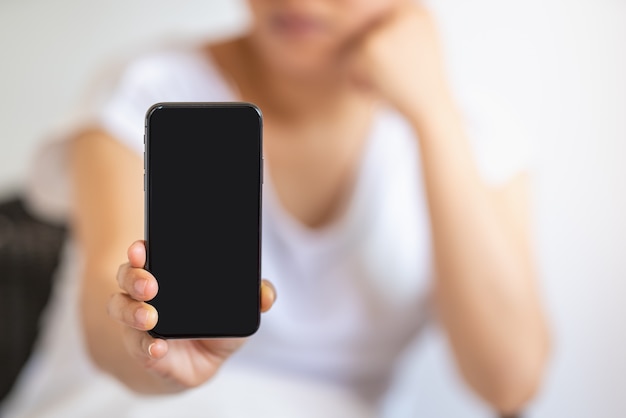 Primo piano della mano della donna che tiene e mostra lo smartphone nero dello schermo in bianco.