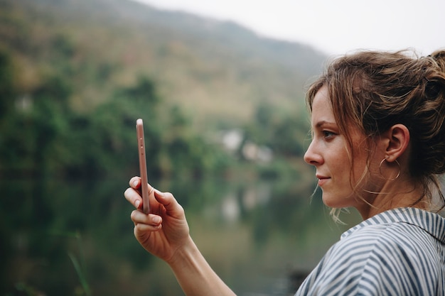 彼女のスマートフォンを上げる女性の手の写真のアップ自然の旅行と観光の概念を撮影する