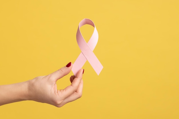 Closeup of woman hand with manicure holding pink ribbon symbol of breast cancer awareness