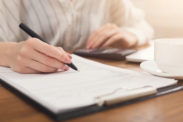 Closeup of woman hand writing in documents and using calculator. Financial background, count and pay an account, copy space, selective focus