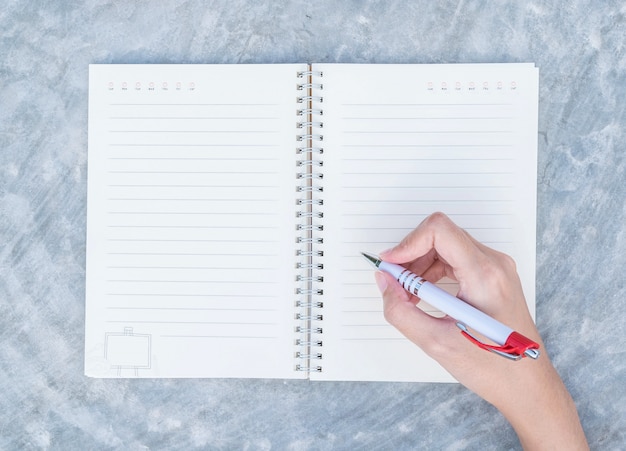 Closeup woman hand writing on note book on concrete desk in top view textured background under day light in the garden