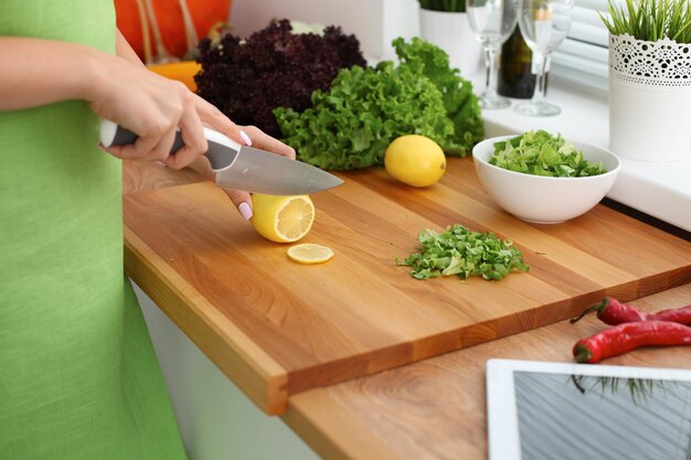 Closeup of woman hands cooking vegetables salad in kitchen Housewife cuts lemon Healthy meal and vegetarian concept