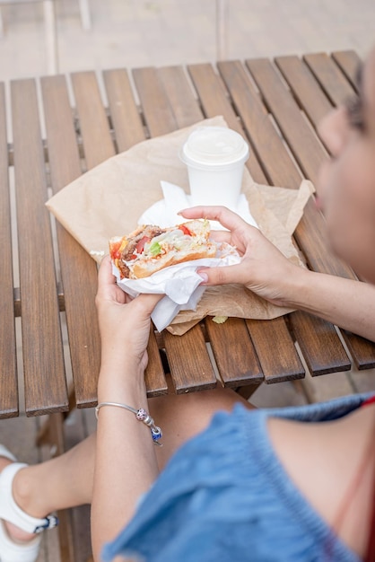 後ろからストリートカフェビューでファーストフードを食べるハンバーガーの女性を保持している女性の手のクローズアップ