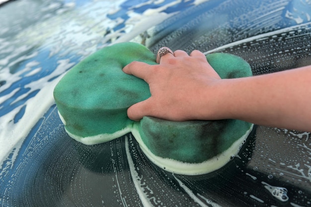 Foto primo piano le mani della donna utilizzando una spugna verde con schiuma di sapone che lava la sua auto moderna