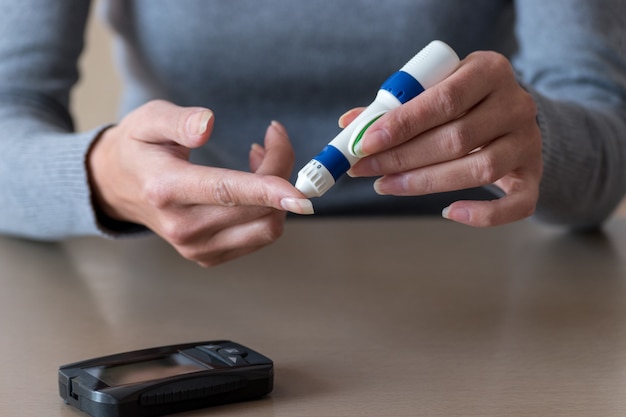 Primo piano delle mani della donna che usano la lancetta sul dito per controllare il livello di zucchero nel sangue mediante il glucometro