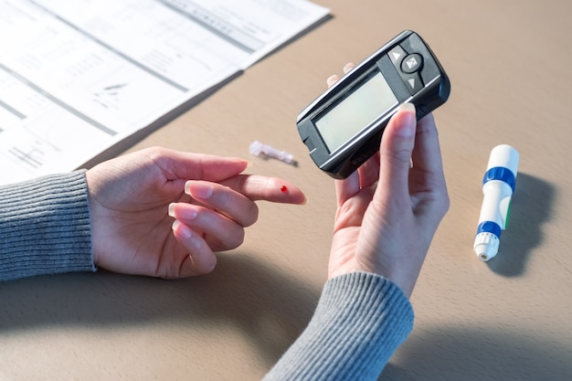 血糖値計で血糖値をチェックするために指にランセットを使用して女性の手のクローズアップ