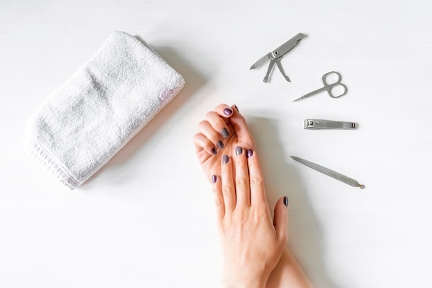 Closeup of woman hands with polished nails and manicure instruments. caucasian woman receiving french manicure at home or at nail salon. manicure, selfcare, beauty procedures yourself.