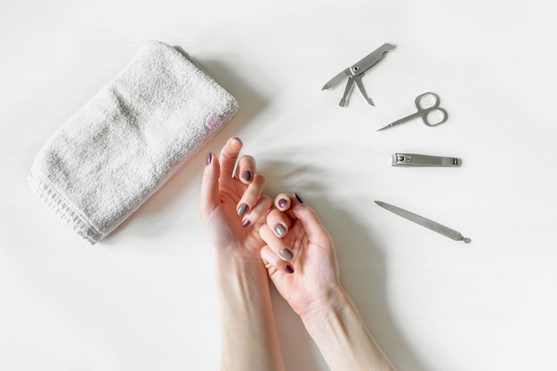 Closeup of woman hands with polished nails and manicure instruments. Young caucasian woman receiving french manicure at home or at nail salon. manicure, selfcare, beauty procedures yourself .