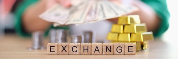 Closeup of woman holding banknotes cash and gold ingots coins on table exchange word on wooden