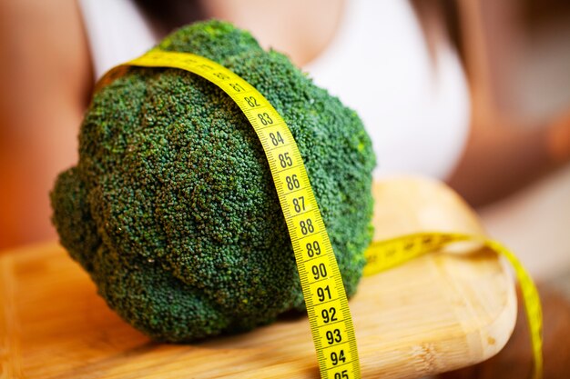 Closeup of woman holding broccoli with string tape to measure