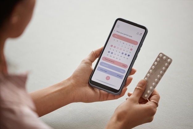 Foto close-up di una donna che tiene in mano un telefono con un'app di calendario e pillole