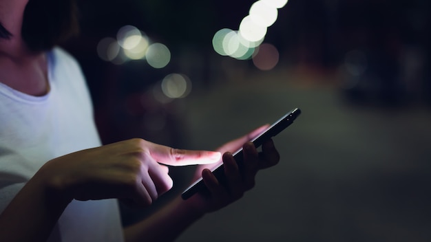 Closeup of woman holding a smartphone at night on street. Technology for communication concept. 