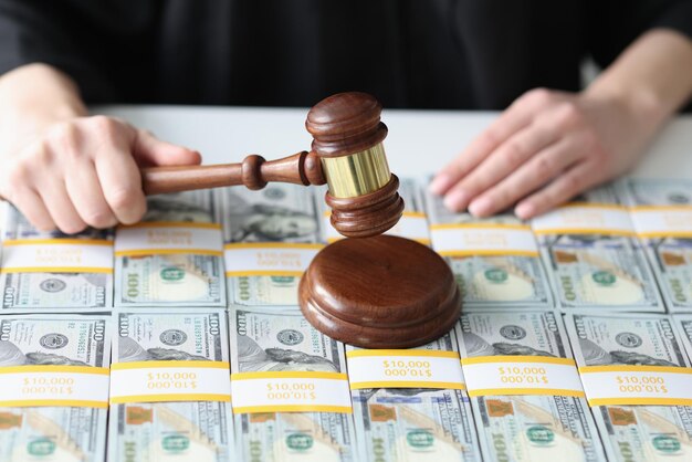 Closeup of woman judge holding wooden gavel pile of dollars on table financial fraud and