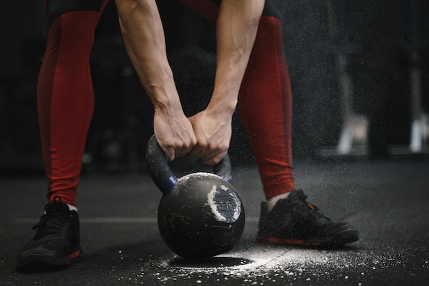 Photo closeup of woman lifting heavy kettlebell at gym